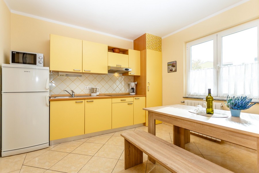 Žltá kuchyňa s jedálenským stolom a lavicami, svetlé obklady na stenách