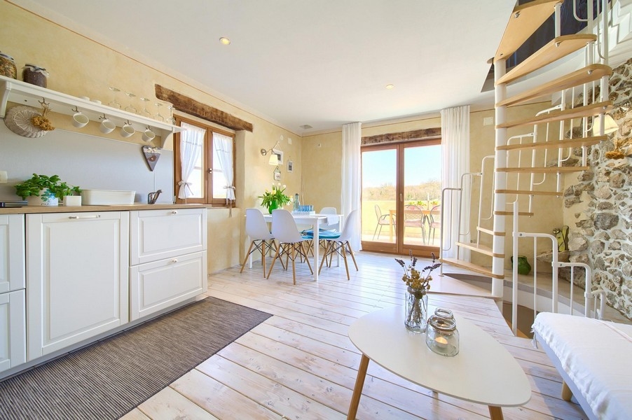 Otvorený obývací priestor s modernou kuchyňou, jedálenským stolom a prístupom na terasu, zariadený svetlým nábytkom.