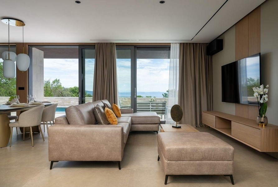 Obývacia izba s veľkými presklenými oknami a výhľadom na bazén