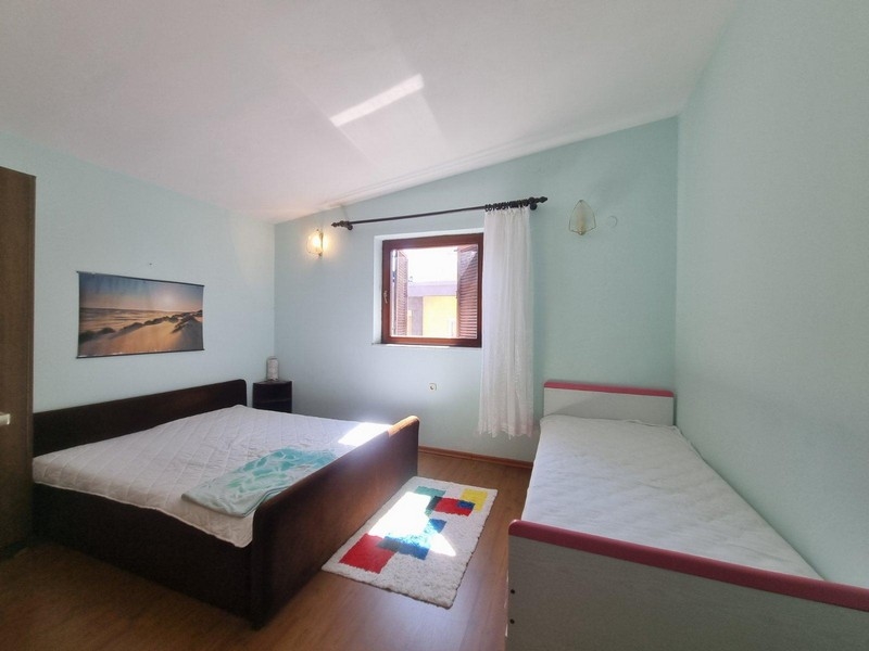 Spálňa s manželskou posteľou a jednolôžkom, svetlé steny a okná s prirodzeným svetlom.