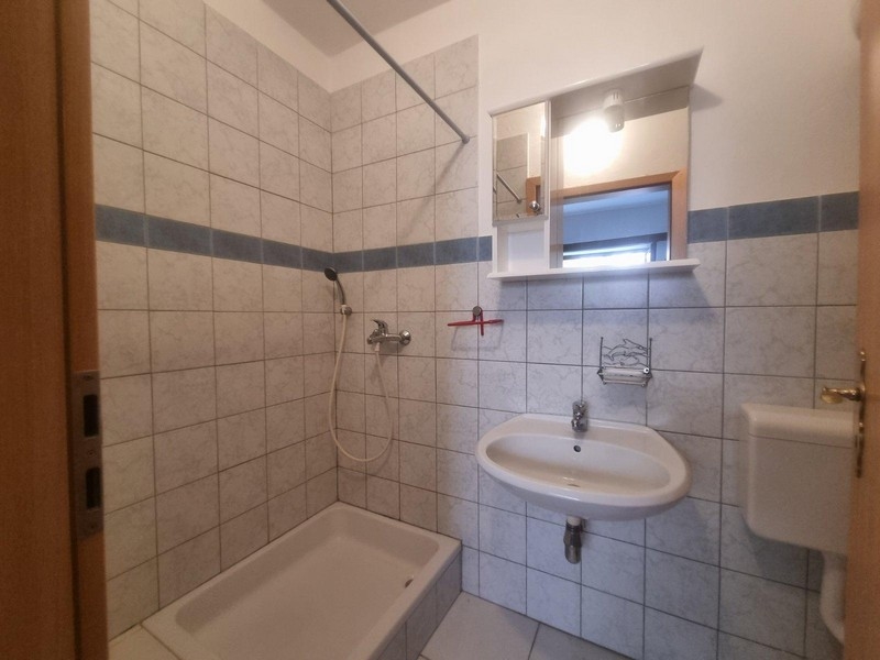 Svetlá kúpeľňa s dlažbou, sprchovým kútom a jednoduchým umývadlom.