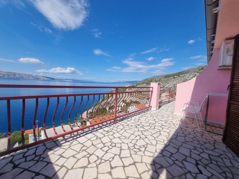 Veľká otvorená terasa s mozaikovými kamennými podlahami, červeným zábradlím a výhľadom na more a okolitú krajinu.