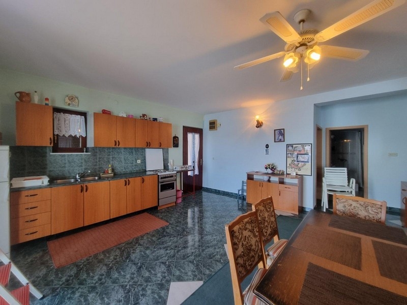 Priestranná kuchyňa s jedálenským stolom, dreveným nábytkom a stropným ventilátorom v presvetlenom prostredí.