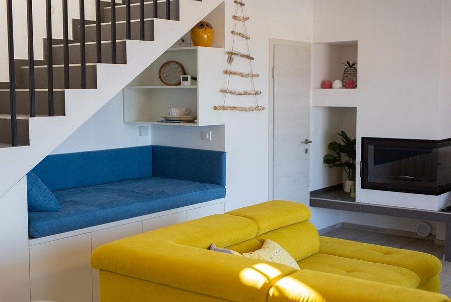 Obývacia izba so žltou pohovkou, modrým posedením pod schodmi, moderný dizajn