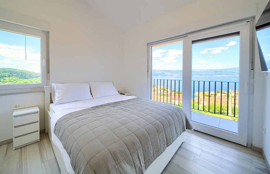 Spálňa s manželskou posteľou a balkónovými dverami, nádherný výhľad na more v pozadí