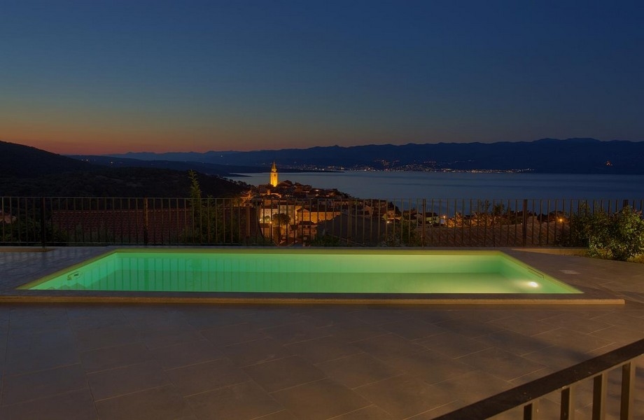 Osvetlený bazén v noci a výhľad na Vrbnik v Chorvátsku.