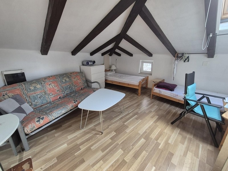 Otvorený obytný priestor v podkroví s dvomi posteľami a drevenými trámami na strope.