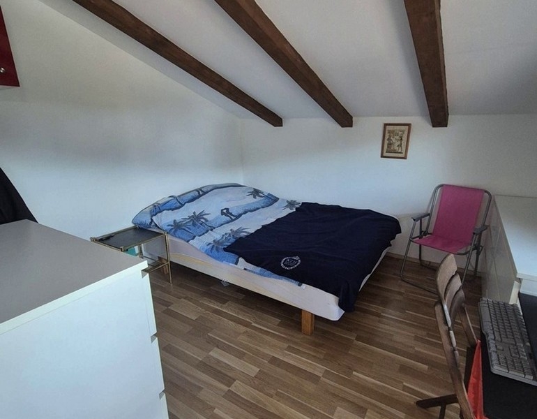 Spálňa v podkroví s drevenými trámami a manželskou posteľou.