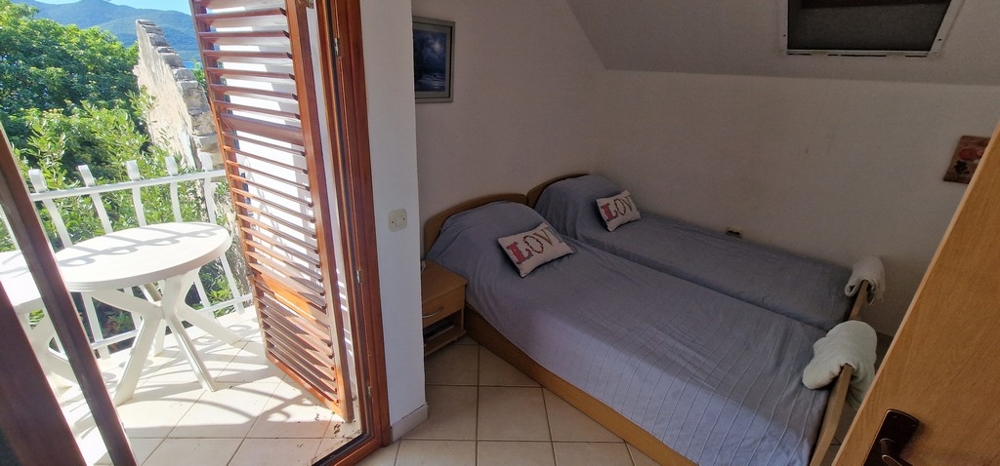 Spálňa s dvoma jednolôžkami pokrytými modrými prikrývkami. K dispozícii je malý balkón s okrúhlym stolom a stoličkami a výhľadom do zelene.