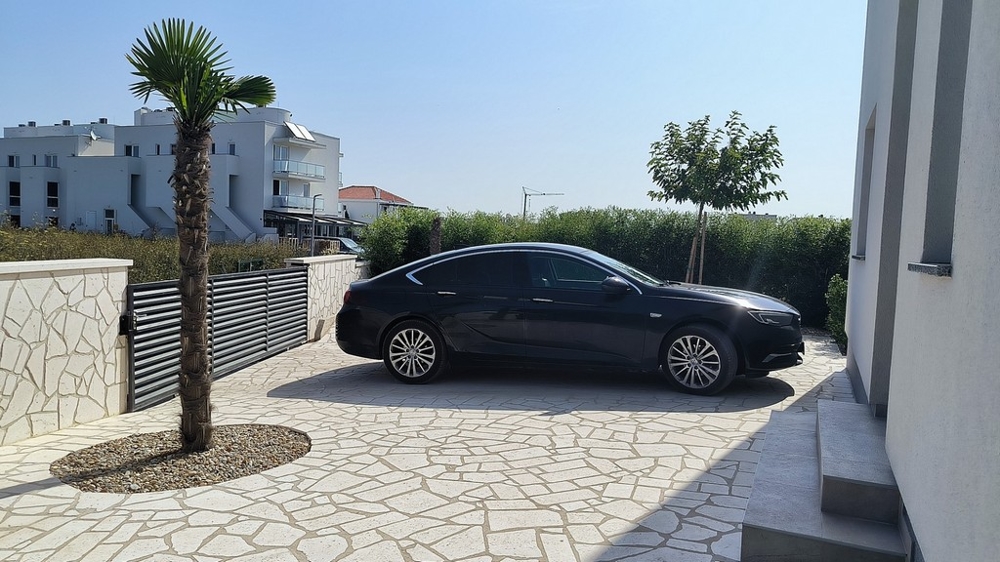 Vchod s autom, palmami a kamenným múrom.