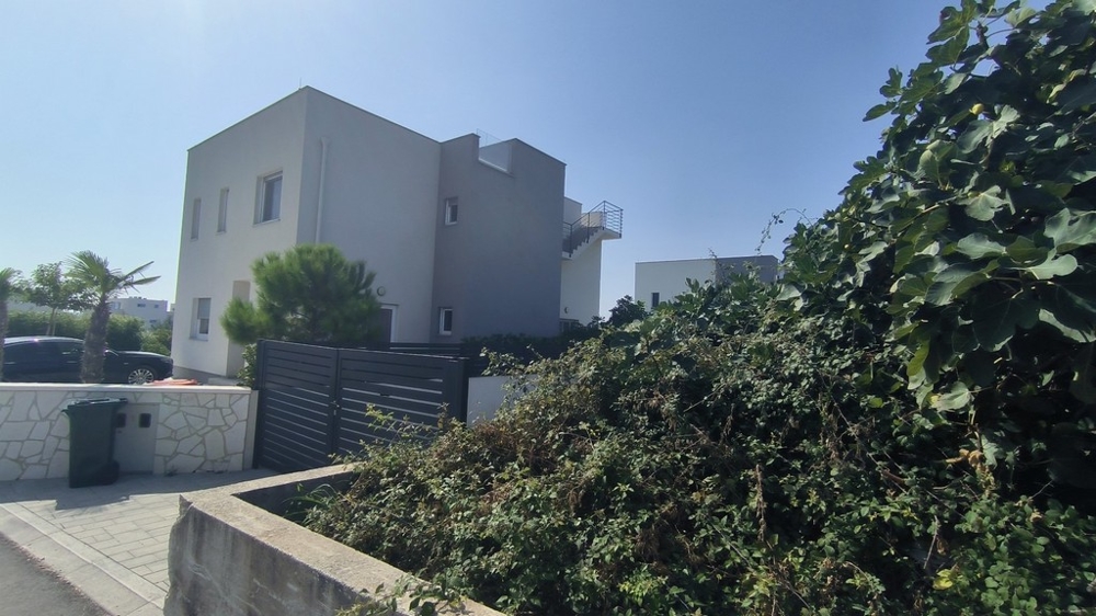 Vonkajší pohľad na moderný dom so zeleným živým plotom a palmami.