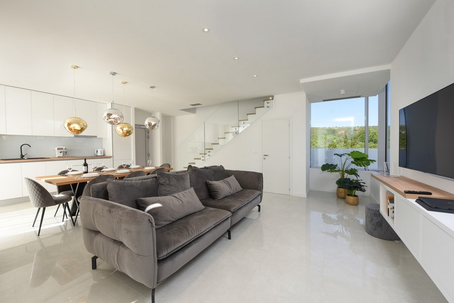 Otvorená obývacia izba s moderným zariadením, sivou pohovkou a výhľadom do prírody.