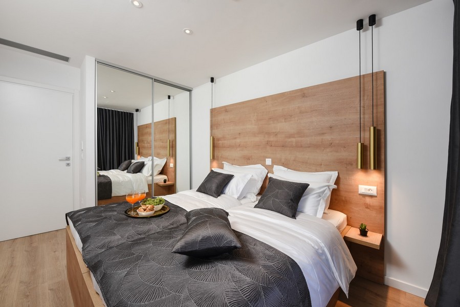 Moderne zariadená spálňa s drevenými prvkami a zrkadlovou skriňou s posuvnými dverami.