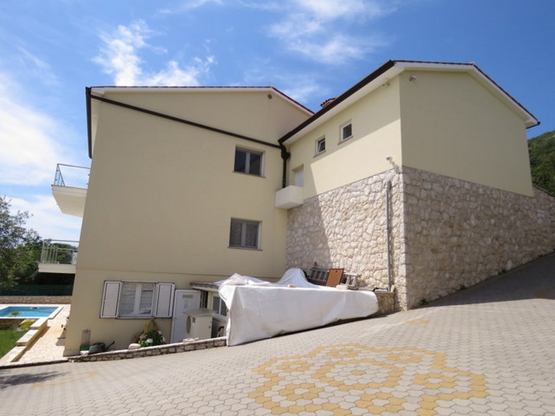 Vonkajší pohľad na dom s vydláždeným parkoviskom a bazénom v pozadí.