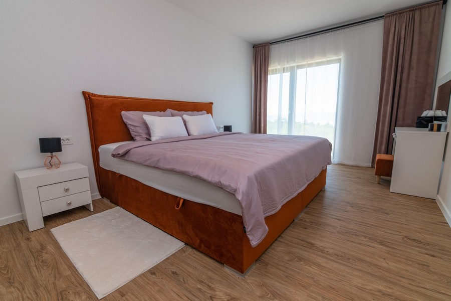 Spálňa s oranžovou posteľou a veľkými oknami