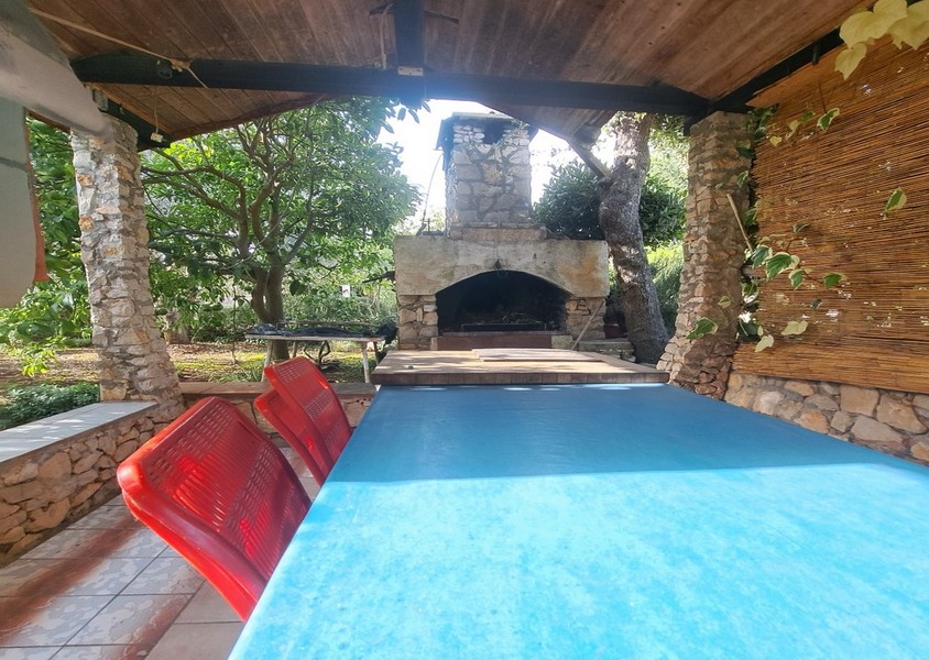 Vonkajší priestor s grilom, stolom a červenými stoličkami.