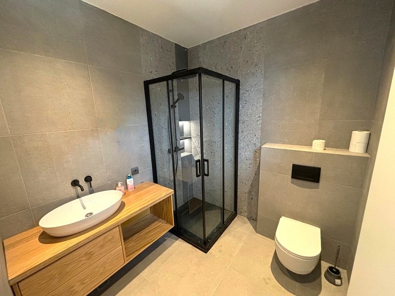 Moderná kúpeľňa so skleneným sprchovacím kútom a dreveným umývadlom