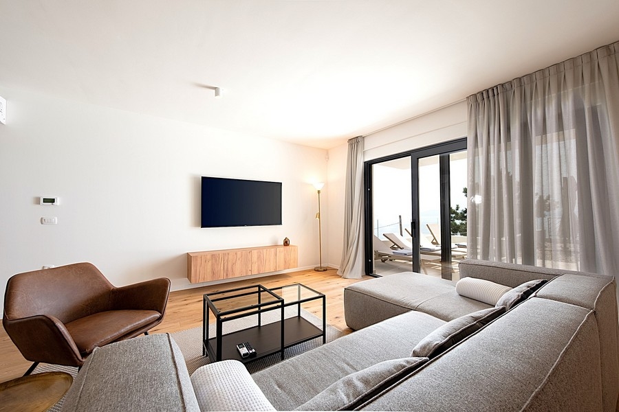 Obývacia izba so sivou pohovkou, TV a vstupom na terasu