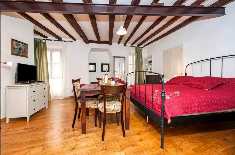 Svetlý apartmán s posteľou, drevenými trámami a stolom