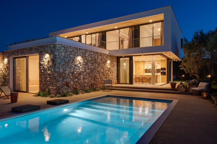 Vila v noci s osvetleným bazénom a fasádou z prírodného kameňa