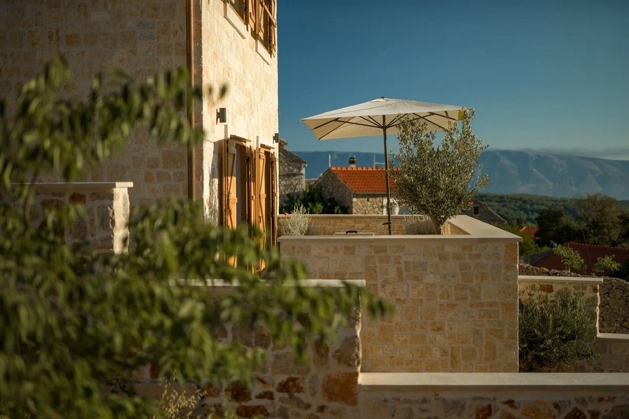 Kamenný dom s terasou a slnečníkom, výhľad na hory