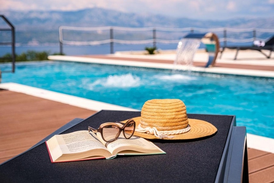 Detailný záber na bazén s ležadlom, klobúkom, okuliarmi a knihou