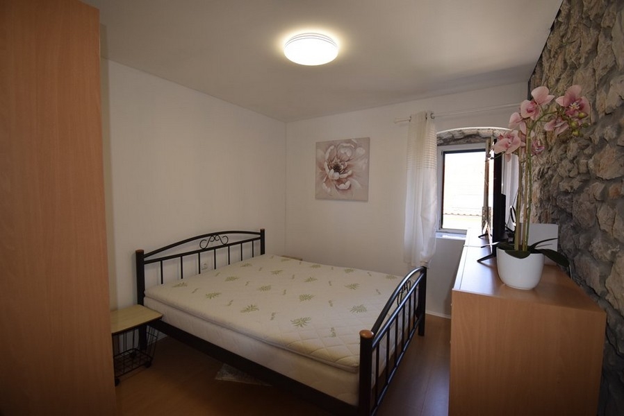 Svetlá spálňa s manželskou posteľou a kamennou stenou