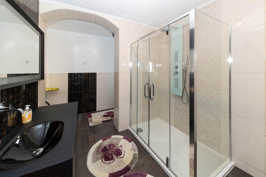 Moderná kúpeľňa s veľkým preskleným sprchovacím kútom a tmavým umývadlom