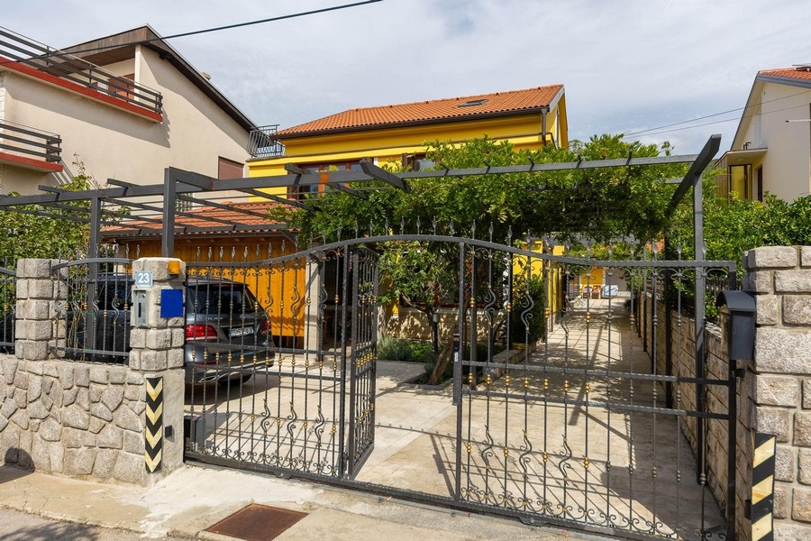 Vstup na pozemok s bránou a žltý dom