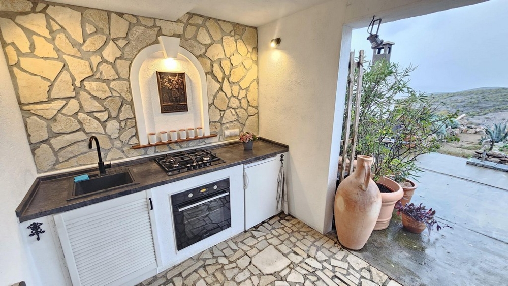 Krytá letná kuchyňa s kamennou stenou a plynovým sporákom