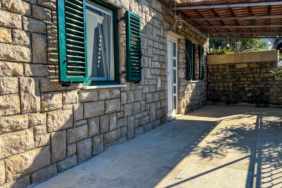 Kamenná terasa so vstupom do domu a zelenými okenicami