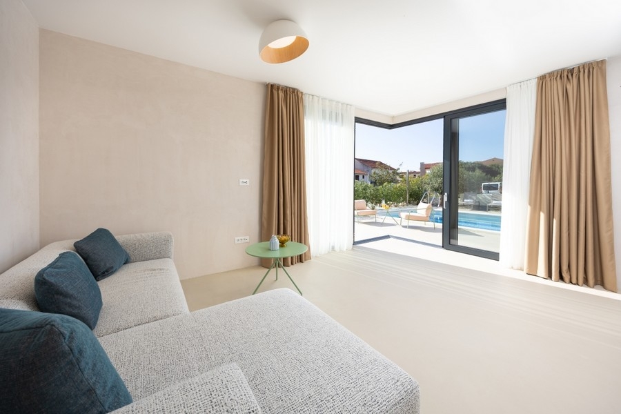 Obývacia izba s pohovkou a výhľadom na terasu a bazén