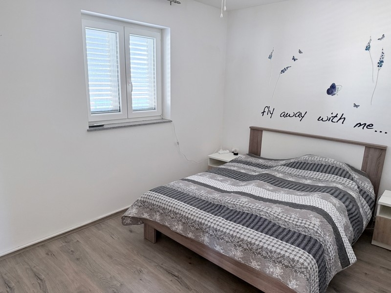 Spálňa s manželskou posteľou a oknom v pokojnej lokalite na ostrove Pag