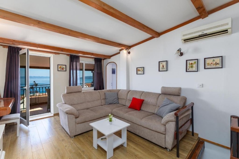 Obývacia izba s rohovou pohovkou a prístupom na balkón s výhľadom na more